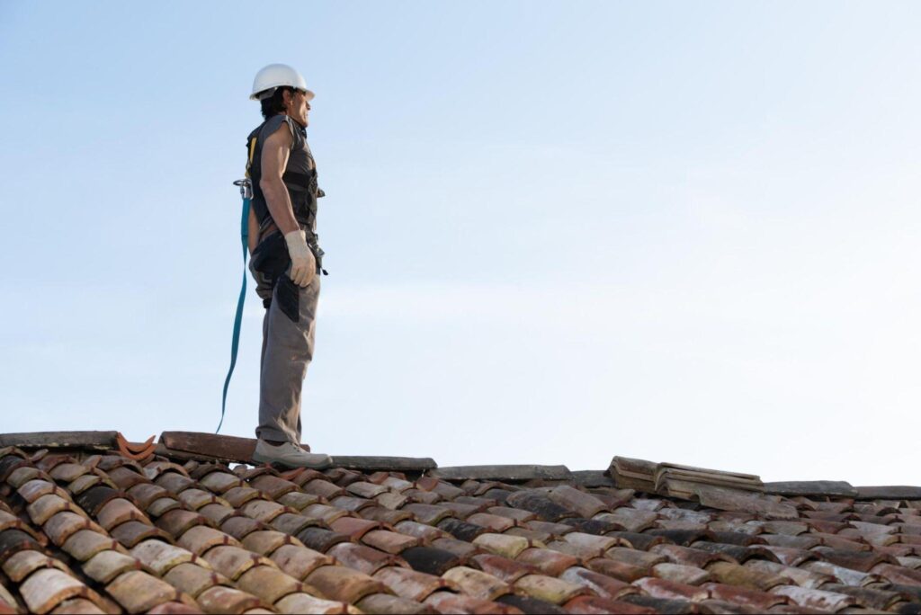 A man stands on the roof of a house, looking out over the surrounding area.