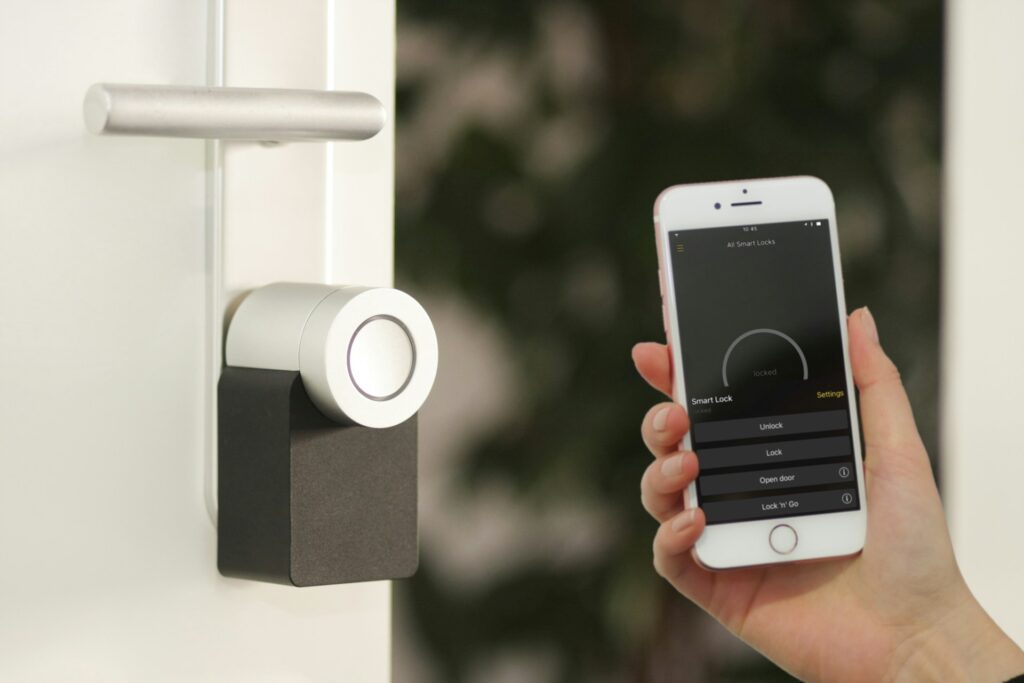 A person’s hand holding a smartphone next to a smart lock with an open smart lock app on the phone screen